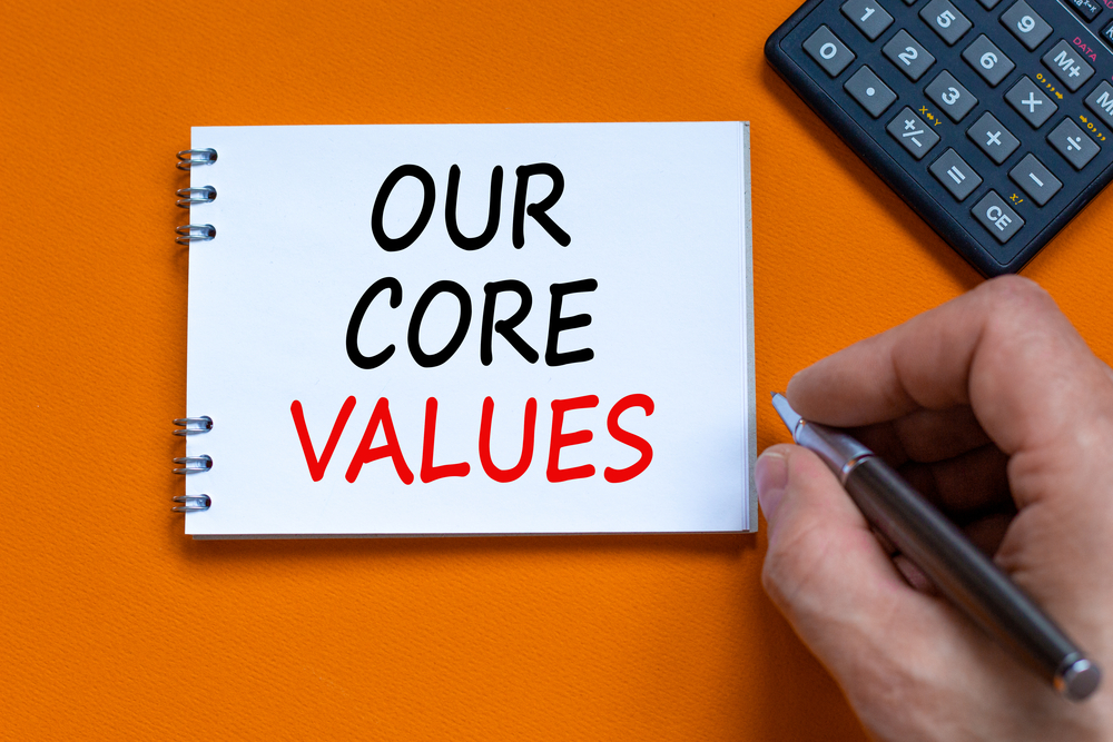 Our core values symbol. Businessman writing words 'Our core values' on white note. Black calculator. Beautiful orange background. Business and our core values concept.