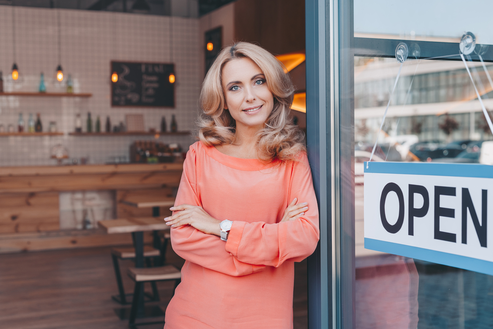 Woman business owner in her shop next to a door that says "Open".